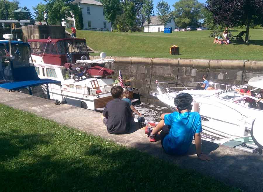 Kids sitting and watching boats crossing Rideau Canal locks during bike & boat bike tours of Ottawa with escape on Sparks