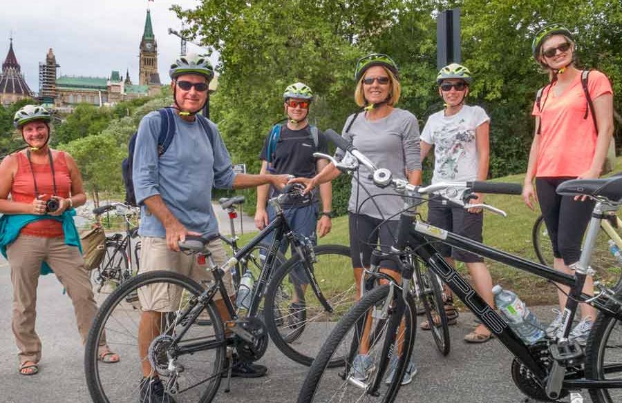 Guests have stopped at Rideau Canal with a view of the Parliament Building during Escape full day guided bike tour in Ottawa