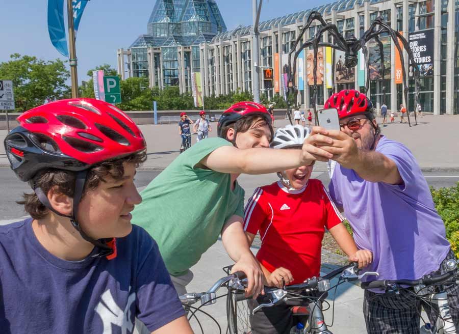 Happy family is taking a selfie in front of Maman, spider at National Art Gallery during express tour by bike in Ottawa