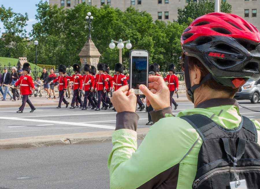 A guest is watching and taking a picture of the change of guard ceremony on Elgin st. during Ottawa highlights bike tour 