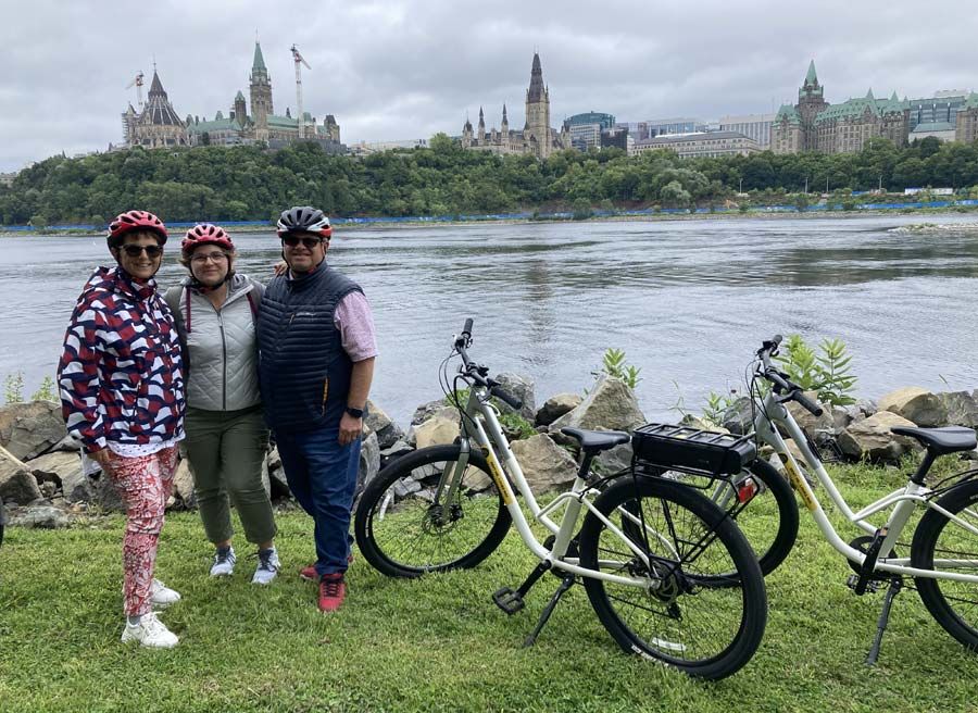 A family has joined Ottawa Electric Bike tour with Escape in Ottawa and have stopped at Ottawa River Pathway to see the view of Parliament Hill.