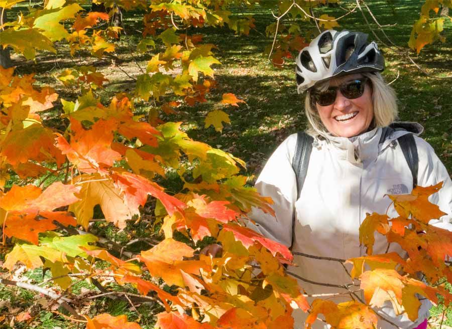 A guest smiling & taking a picture with Fall colours in Ottawa park during Ottawa multi-day cycling tour by Escape on Sparks