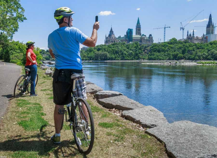 Guests stop at bike path to take pictures of Ottawa River and Parliament Building during a private Ottawa bike tour with Escape Tours Rentals