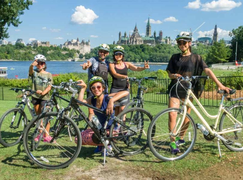 Family enjoying Ottawa express bike tour with a view of the Parliament Building landmark from Ottawa bike trails with escape tours rentals