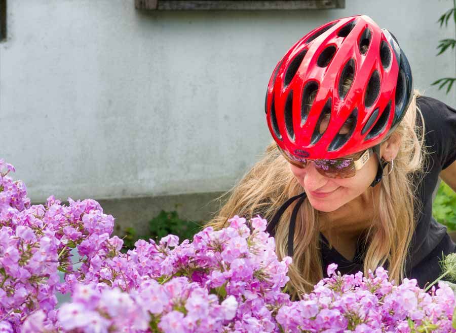 A woman is visiting Ottawa gardens and smelling pink flowers during Escape garden promenade self-guided bike tour in Ottawa