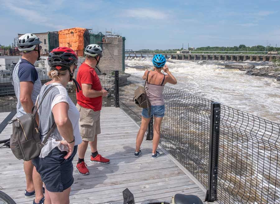 Tour participants are enjoying the view and taking picture of Chaudiere Falls during Ottawa highlights bike tour by Escape