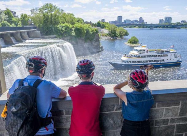 Guests are taking an Escape Ottawa bike & boat tour and stop at Rideau Falls Ottawa landmark to watch a boat cruise