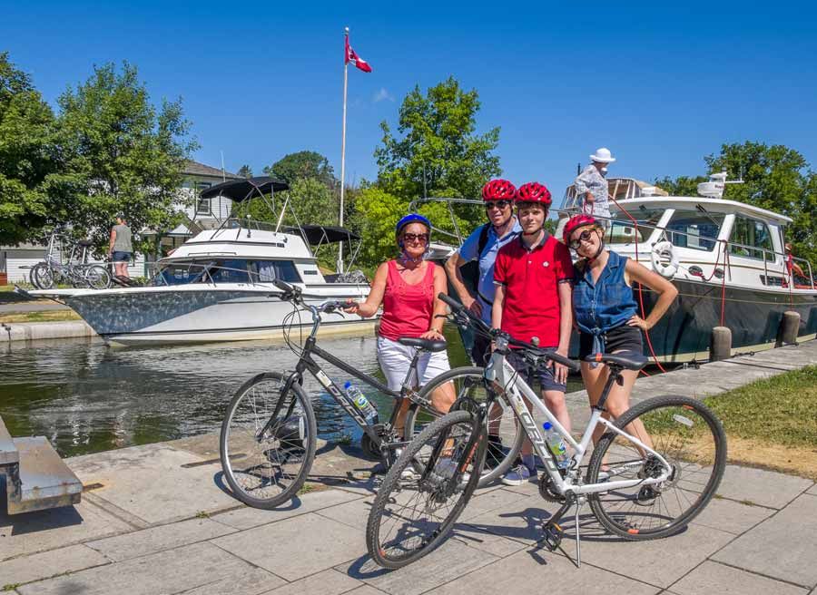 Family is taking a picture next to boats crossing Rideau Canal during bike & boat bike tours of Ottawa with escape on Sparks st.