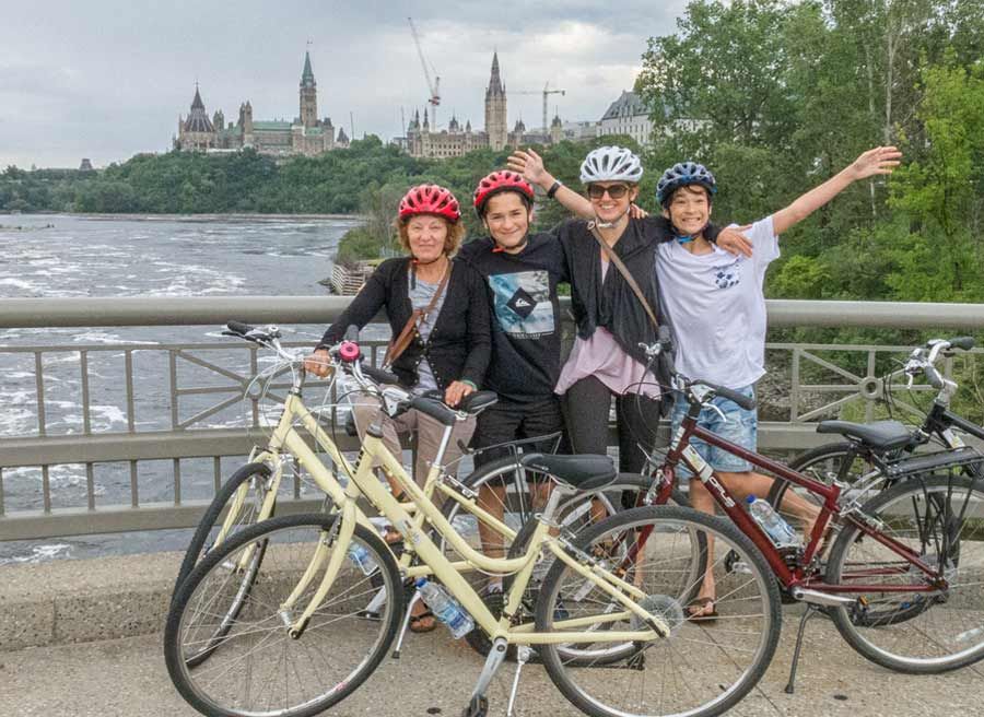 Family is biking on Ottawa river pathway with parliament building view during their Express tour by bike in Ottawa 