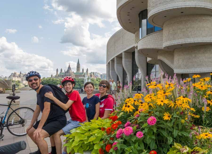 A family is taking a picture at the museum of History lookout with a the parliament view during their private Best of Ottawa bike tour with Escape