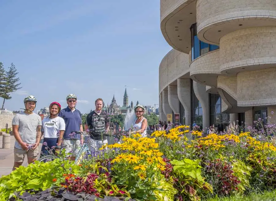 A small- group of tour guests taking a picture in front of a flower garden at History museum during Escape garden bike tour