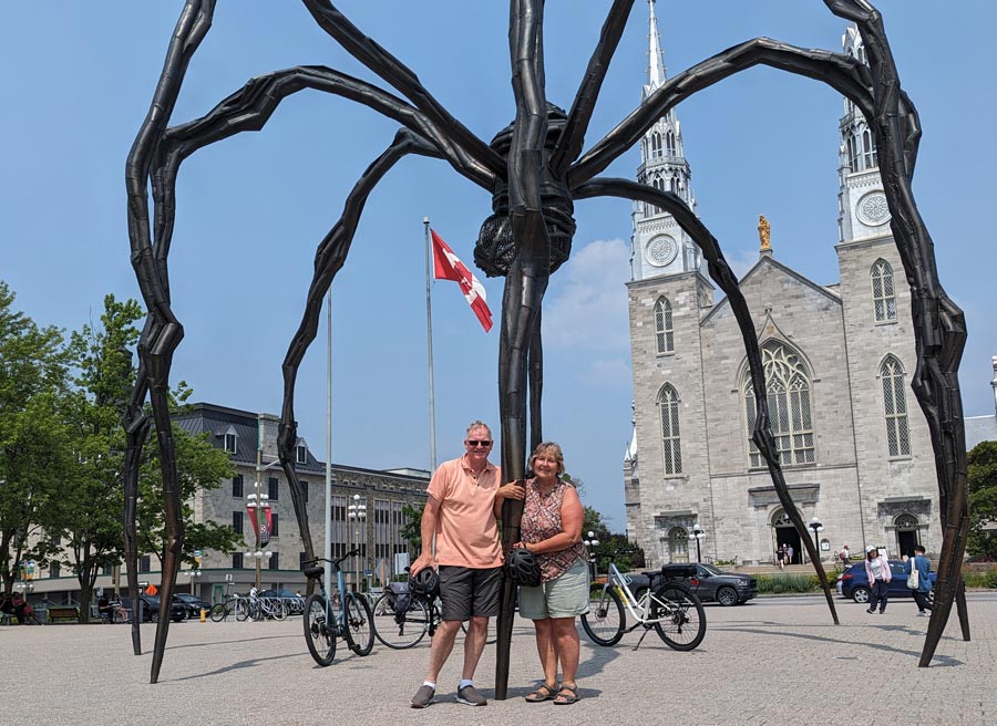 A couple has joined a private Ottawa Electric Bike tour with Escape in Ottawa and have stopped at Maman status for taking pictures and for sightseeing