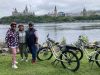 A family has joined Ottawa Electric Bike tour with Escape in Ottawa and have stopped at Ottawa River Pathway to see the view of Parliament Hill.